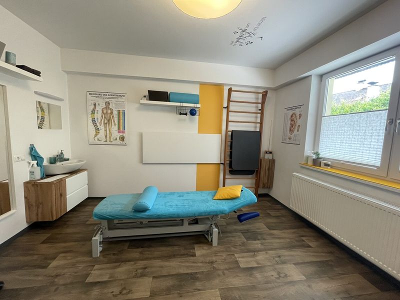 Behandlungsraum mit Therapieliege und anatomischen Postern